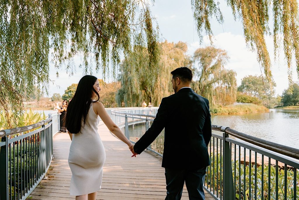 Fiancé's hold hands walking over a bridge at the Chicago Botanic Gardens.
