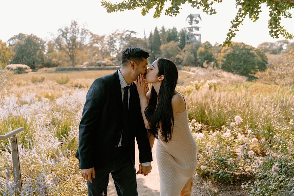 A couple walks and kisses towards the camera surrounded by prairie and flowers at the Chicago Botanic Gardens.