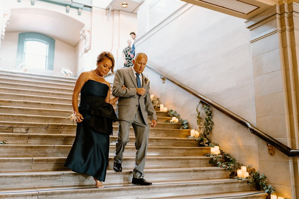 The parents of the groom walk down the decorated staircase of Joliet Union Station framed by greenery and flowers.