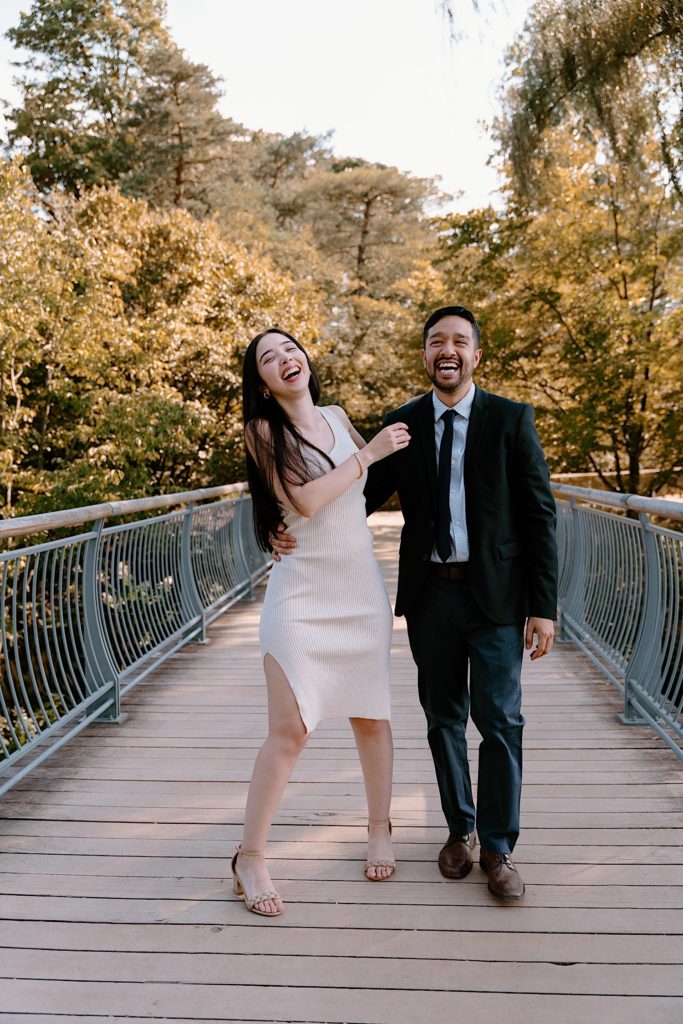 A couple holds one another while walking towards the camera and laughing on a bridge at the Chicago Botanic Gardens.