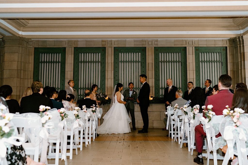 A bride and groom during their ceremony at Joliet Union Station surrounded by their guests.