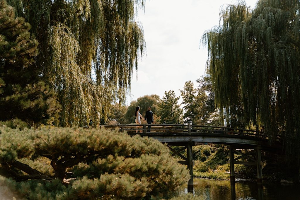 A couple holds hands while walking with one another on a bridge at the Chicago Botanic Gardens.