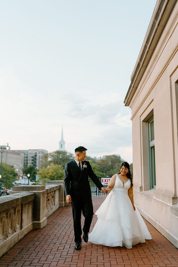 A bride and groom take wedding portraits together on the balcony at Joliet Union Station walking together towards the camera.