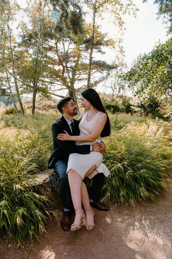 A fiancée sits on her fiances lap during their engagement session at the Chicago Botanic Gardens