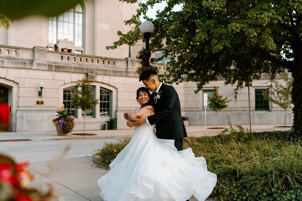 A bride and groom stand in the gardens outside of Joliet Union Station during their wedding portraits dancing together.