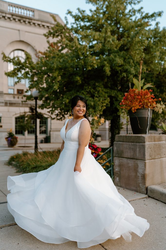 A bride twirls her dress smiling at her groom outside of her Illinois wedding venue.