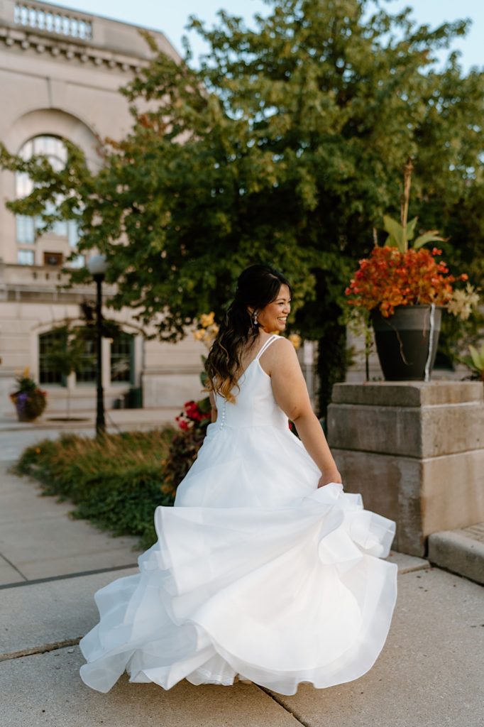 A bride twirls her dress smiling at her groom outside of her Illinois wedding venue.