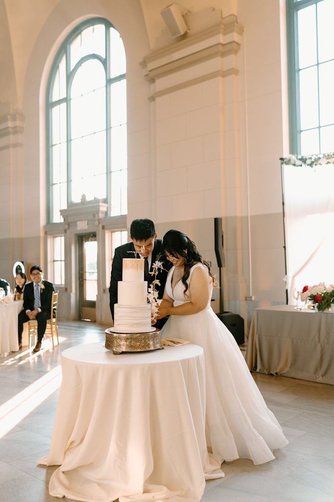 The bride and groom go to cut their cake at the reception at Joliet Union Station celebrating with their guests.