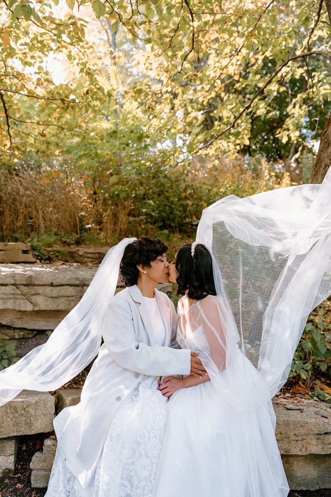 Brides sit together kissing and celebrating their marriage after their eloping at Alfred Caldwell Lily Pool.