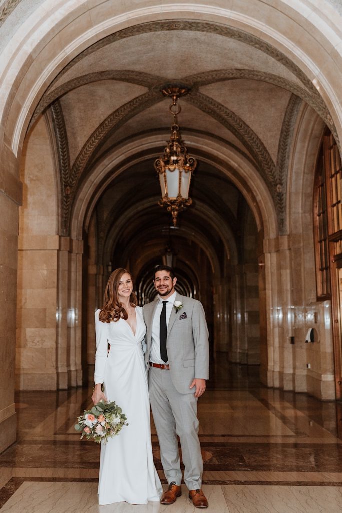 A bride and groom smile at the camera inside Chicago's city hall after eloping. 