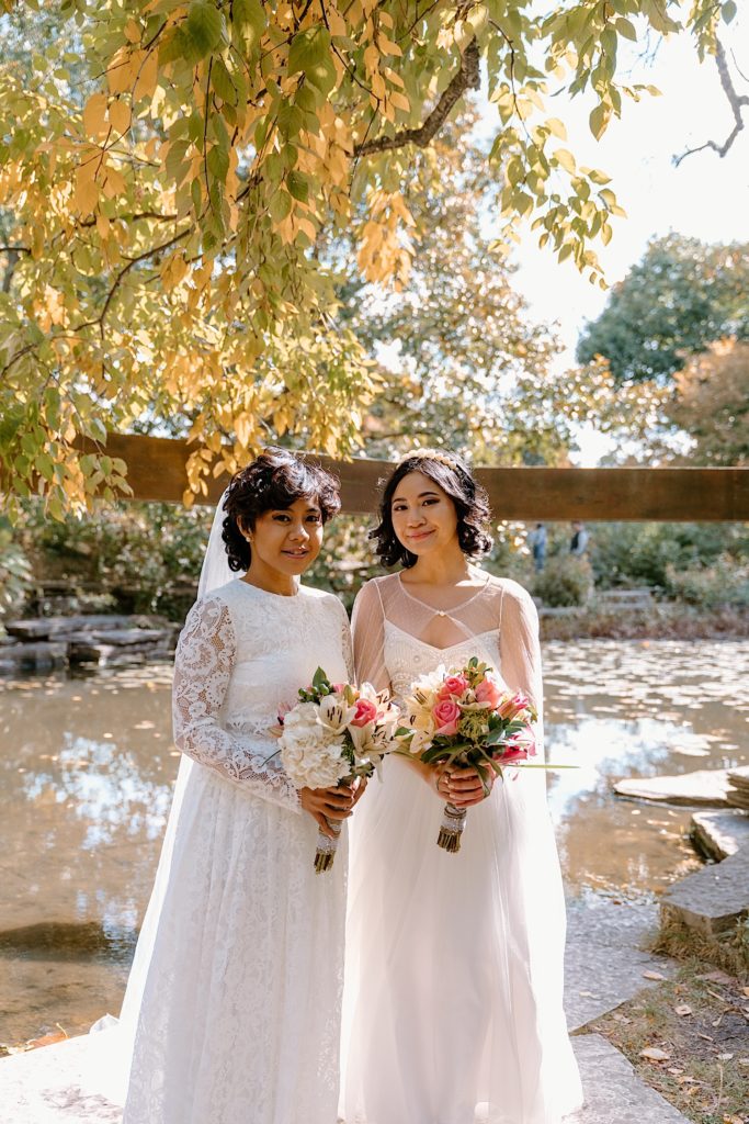 Brides stand together smiling at the camera during their elopement at Alfred Caldwell Lily Pool.