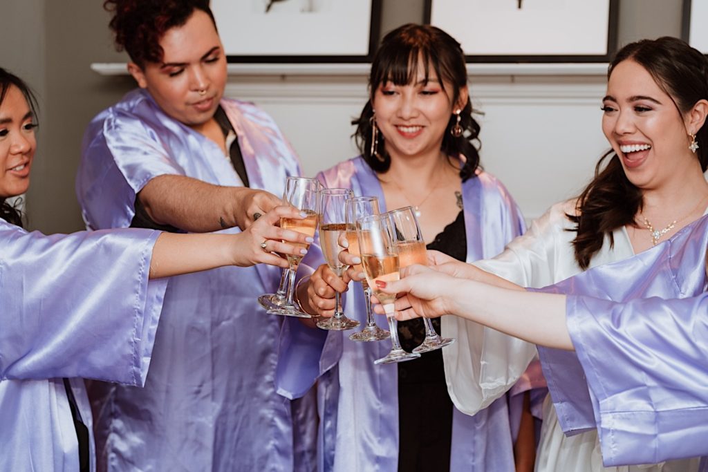 The bridal party clinks their glasses while getting ready with silk robes during their Chicago wedding.