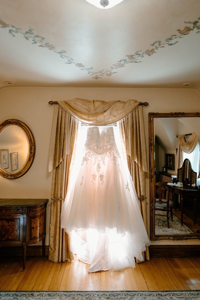 The brides dress hanging in the window inside the dressing room of the Grove Redfield Estate.