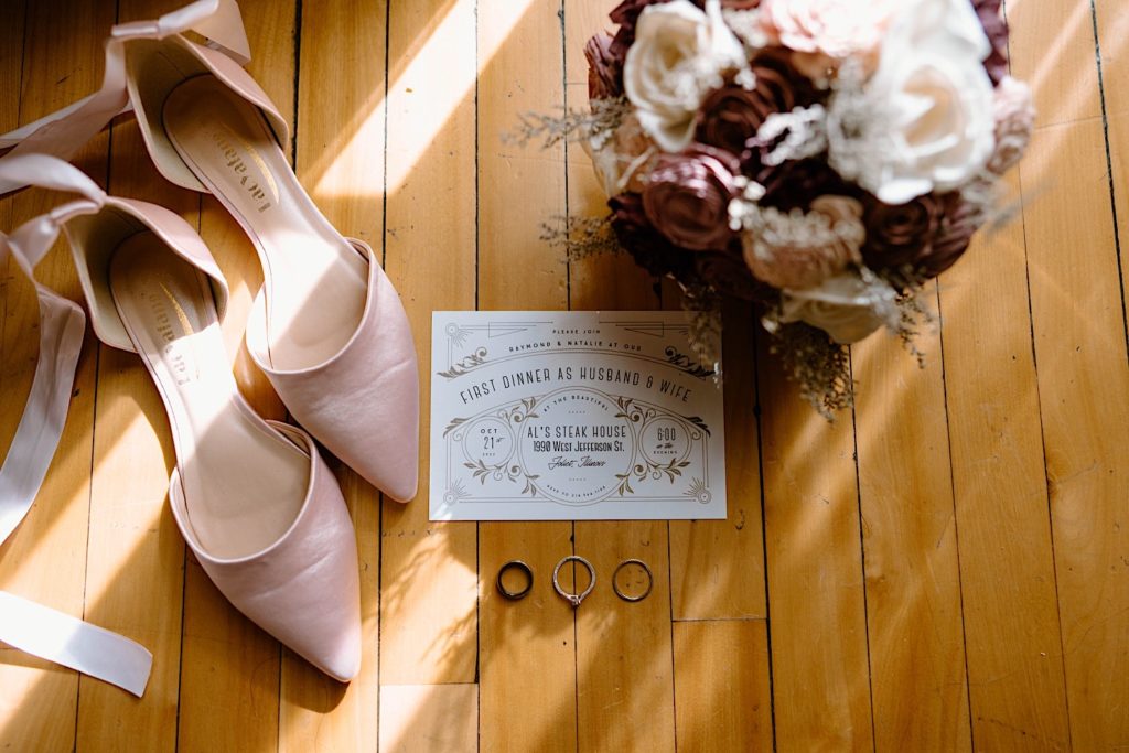 The bride and grooms wedding details and invitation.  Pink shoes, with a pink bouquet and a custom invitation.