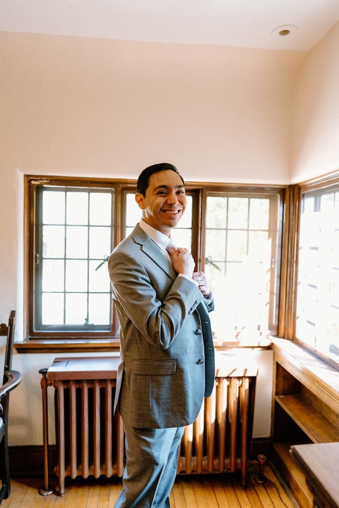 A groom gets ready and smiles at the camera in the getting ready space of the Grove Redfield Estate.
