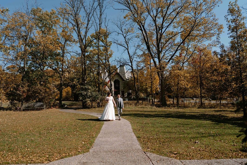 A bride and groom walk holding hands in the fall at their elopement at the Grove Redfield Estate.