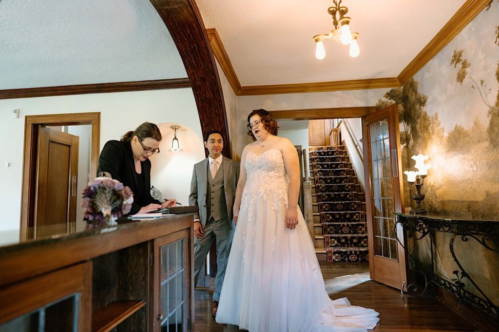 A bride and groom sign their marriage license with their officiant after their elopement ceremony at the Grove Redfield Estate.