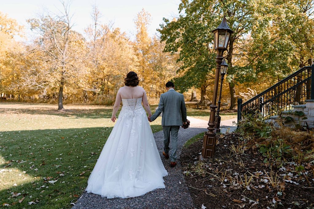 The bride and groom walk along a path at the Grove Redfield Estate Holding hands taking their wedding portraits