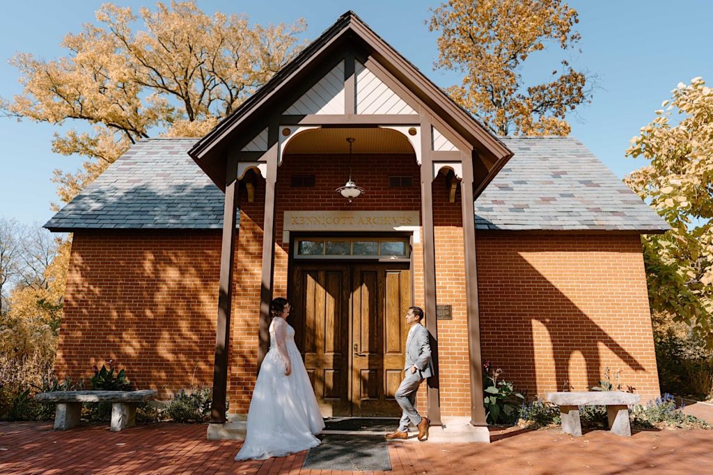 A bride and groom stand in front of the Grove Redfield Estate in the fall after their elopement ceremony.