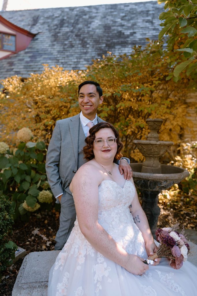 A bride and groom sit in front of the Grove Redfield Estate in the fall after their elopement ceremony.