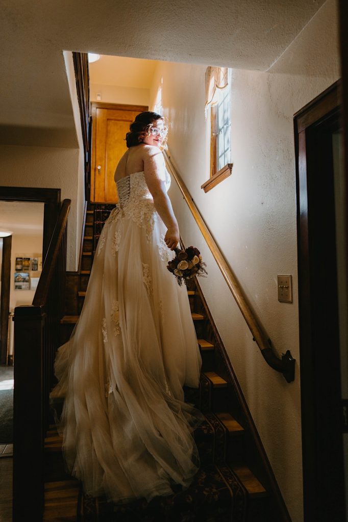 A bride stands in the stairway showing off her dress with a long train at the Grove Redfield Estate 