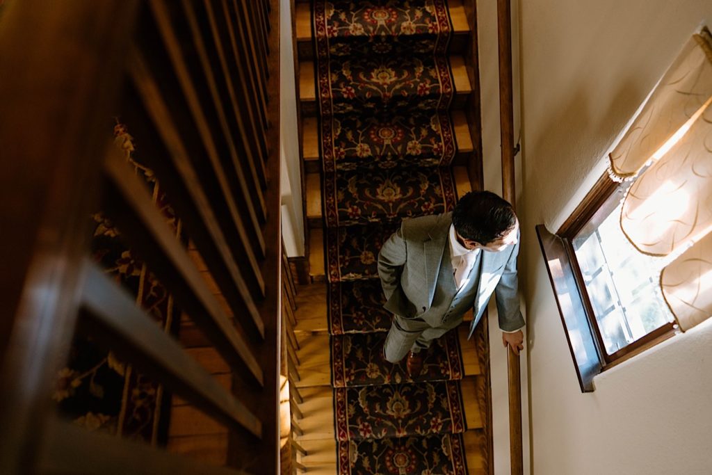 A groom stands in the stairway looking out the window at the Grove Redfield Estate 