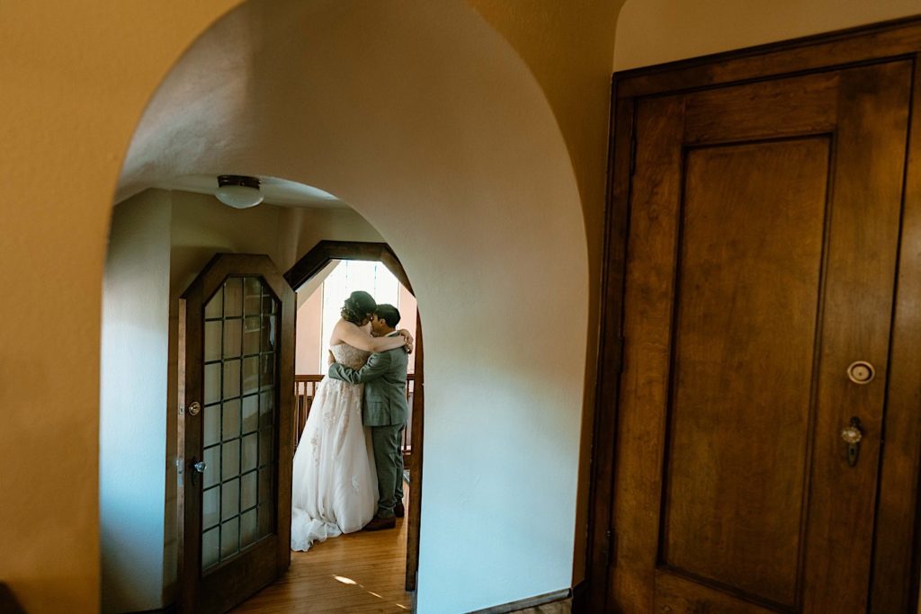A bride and groom stand holding one another through two doorways after their elopement at the Grove Redfield Estate
