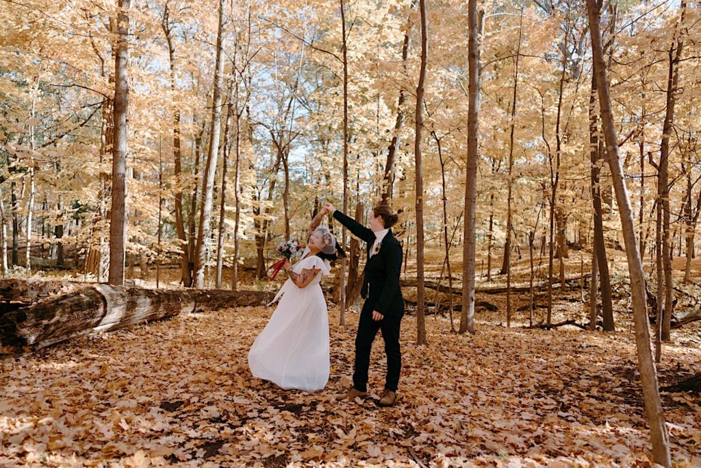 A groom twirls his bride in a forest of Illinois surrounded by yellow leaves during their fall elopement.
