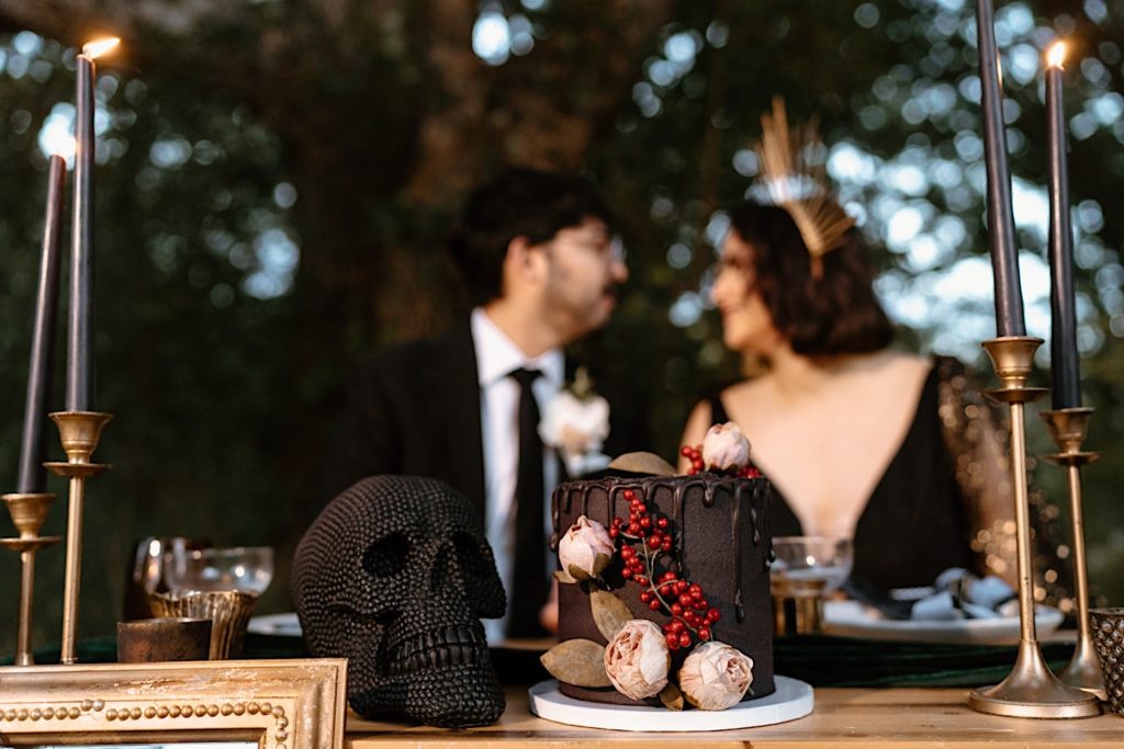 A bride and groom sit behind their wedding cake with a gothic theme.