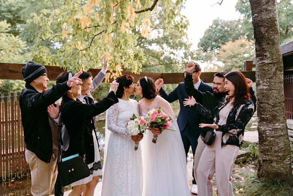 Brides kiss one another surrounded by their loved ones at the Alfred Caldwell Lily Pool.