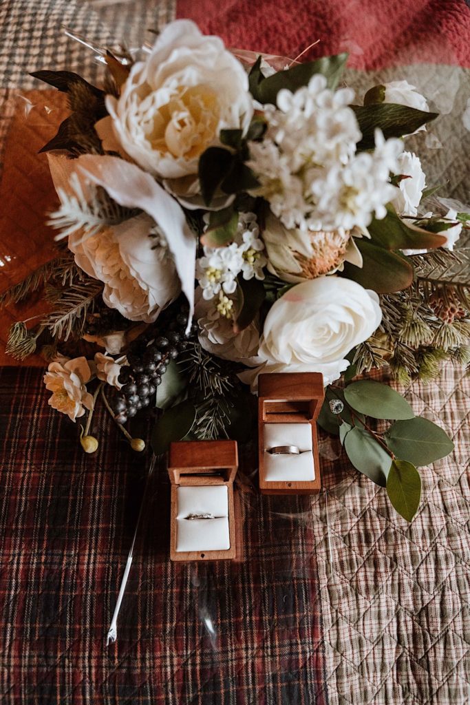 Wooden ring boxes sitting in front of a beautiful bouquet with white roses and berries.