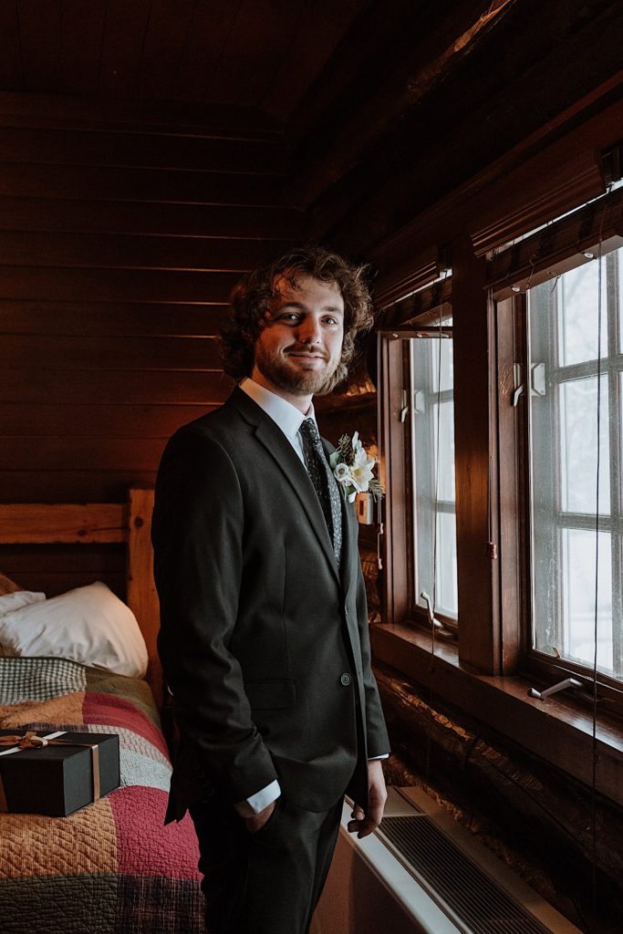 A groom looks directly at the camera smiling in front of a window before his elopement at Starved Rock State Park.