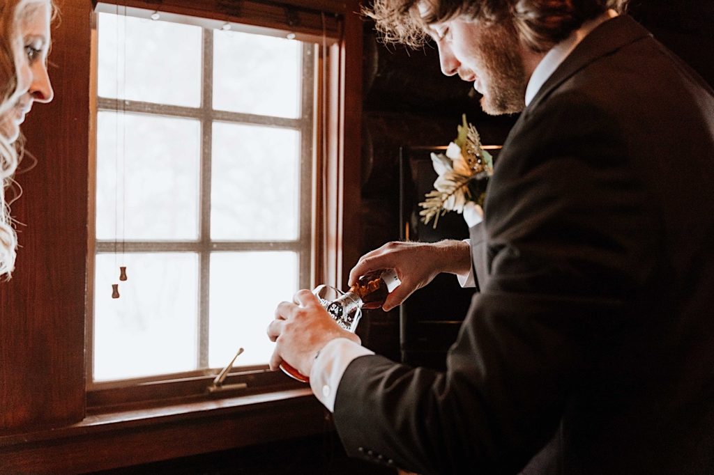 A groom pours beer into a glass before going out to take portraits for their winter elopement at Starved Rock National Park