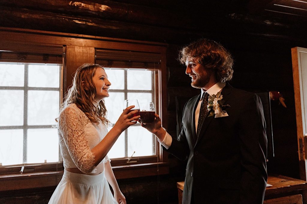A bride and groom clink their glasses of beer while smiling at one another before their elopement at Starved Rock National Park.