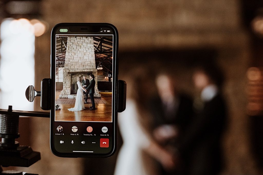 A bride and groom stand during their wedding ceremony at a cabin in Starved Rock National Park while their guests watch via zoom.