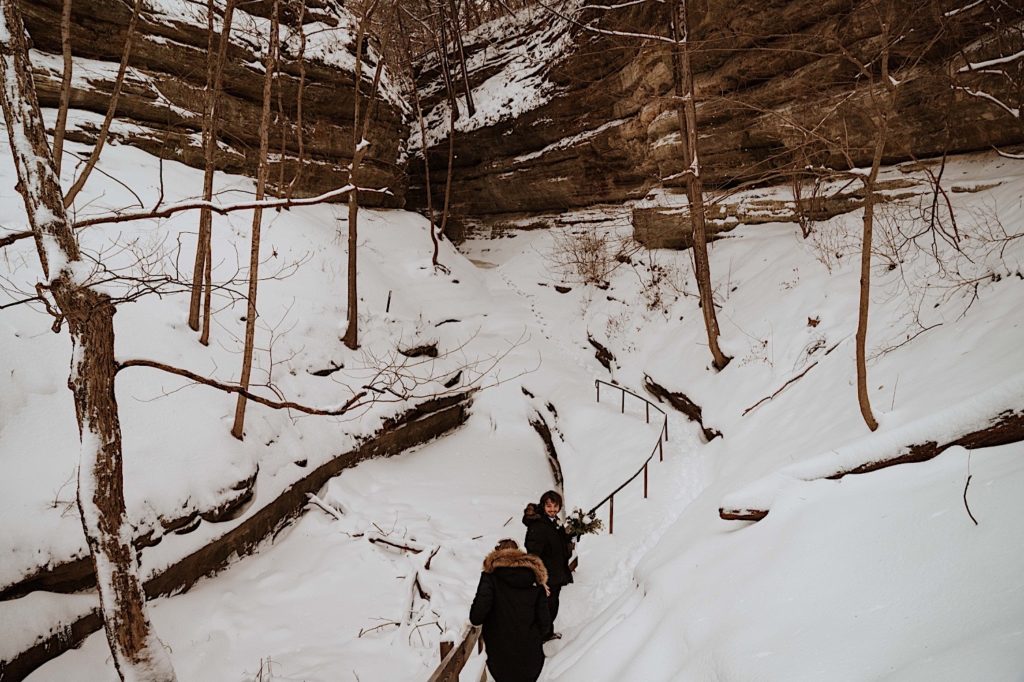 A bride and groom walk along a snow covered trail during their winter elopement at Starved Rock National Park.