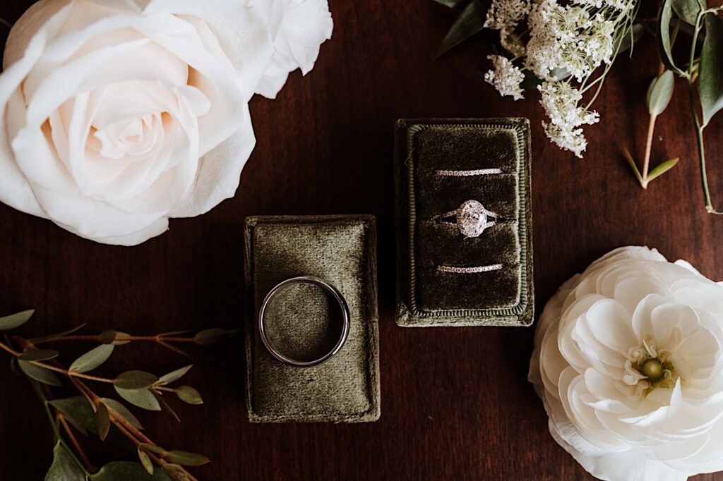 Wedding rings in an olive green velvet box surrounded by white flowers.