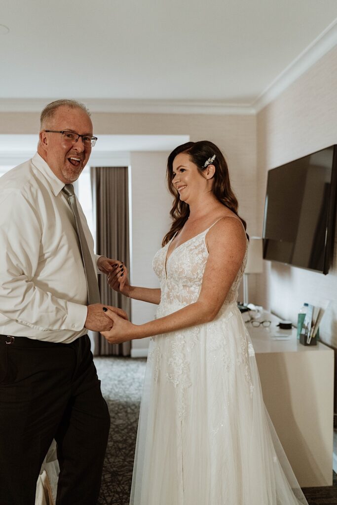 The bride holds her fathers hands smiling with him before leaving for her wedding ceremony in Chicago