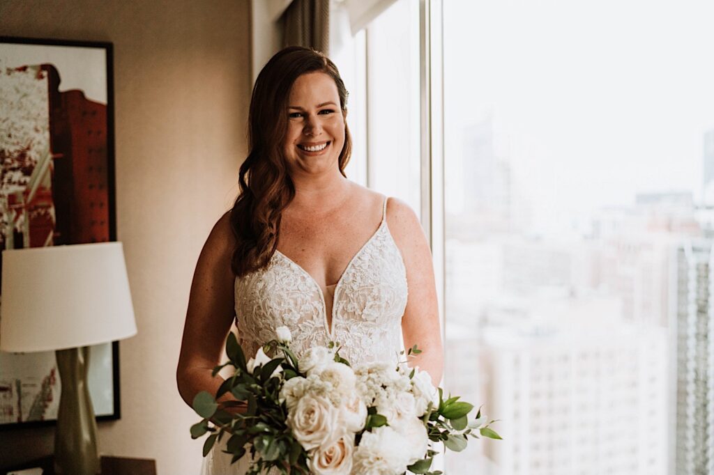 A bride holds her bouquet of white roses standing next to a window in her Chicago hotel before her wedding at the 95th floor.