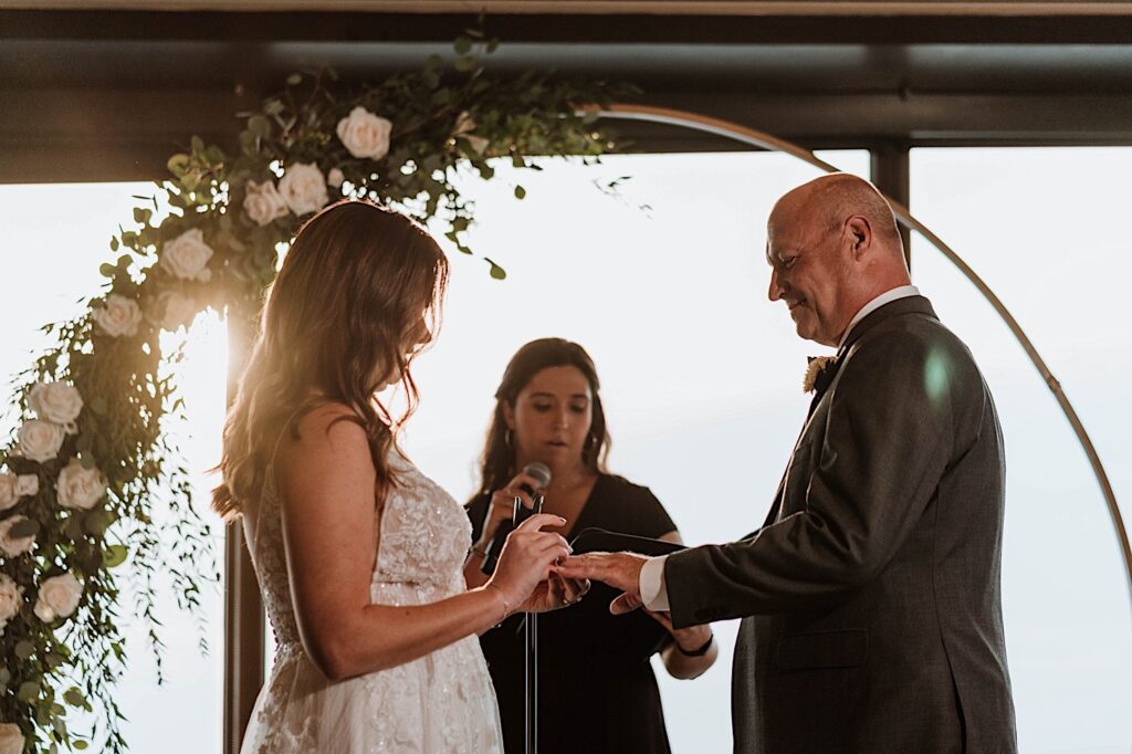 A bride puts a wedding ring on her groom during their wedding ceremony overlooking the city of Chicago in the Signature Room on the 95th floor.