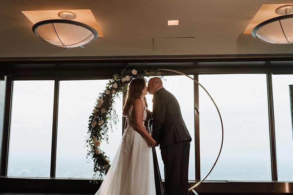 A bride and groom kiss during their wedding ceremony overlooking the city of Chicago in the Signature Room on the 95th floor.