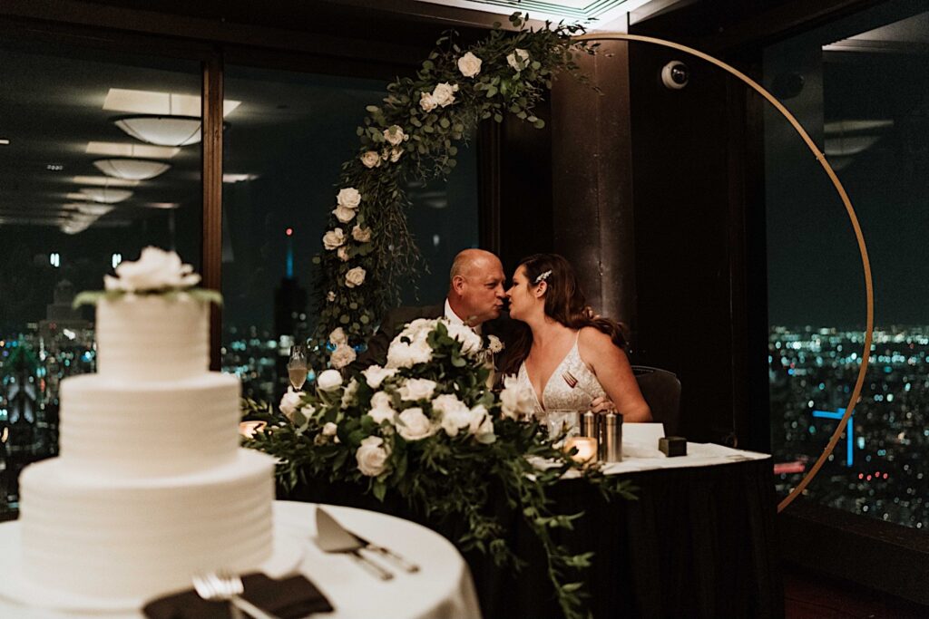 A bride and groom kiss during their dinner at their wedding reception on the 95th Floor in the John Hancock Building.
