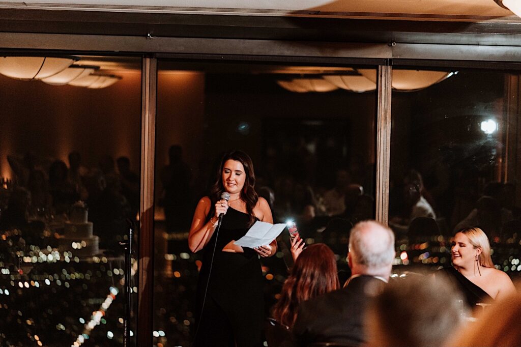 A guest gives a speech at a wedding in front of a window overlooking the city of Chicago