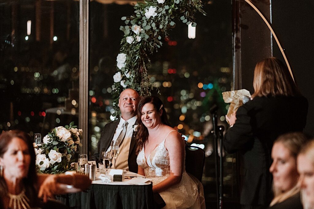 A bride and groom laugh during a speech at their wedding on the 95th floor Signature Room.  