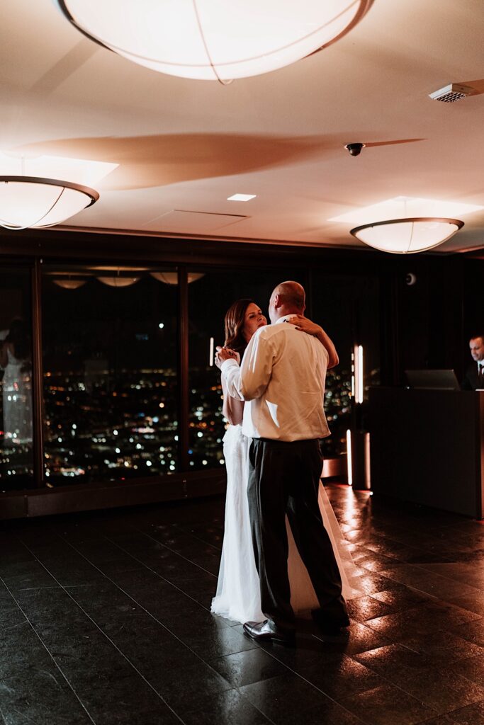 A bride and groom have their first dance overlooking the Chicago night time sky.