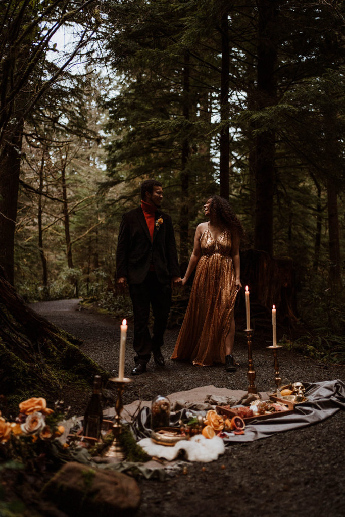 A couple walks to enjoy their dinner in the forest on the Oregon coast for their elopement
