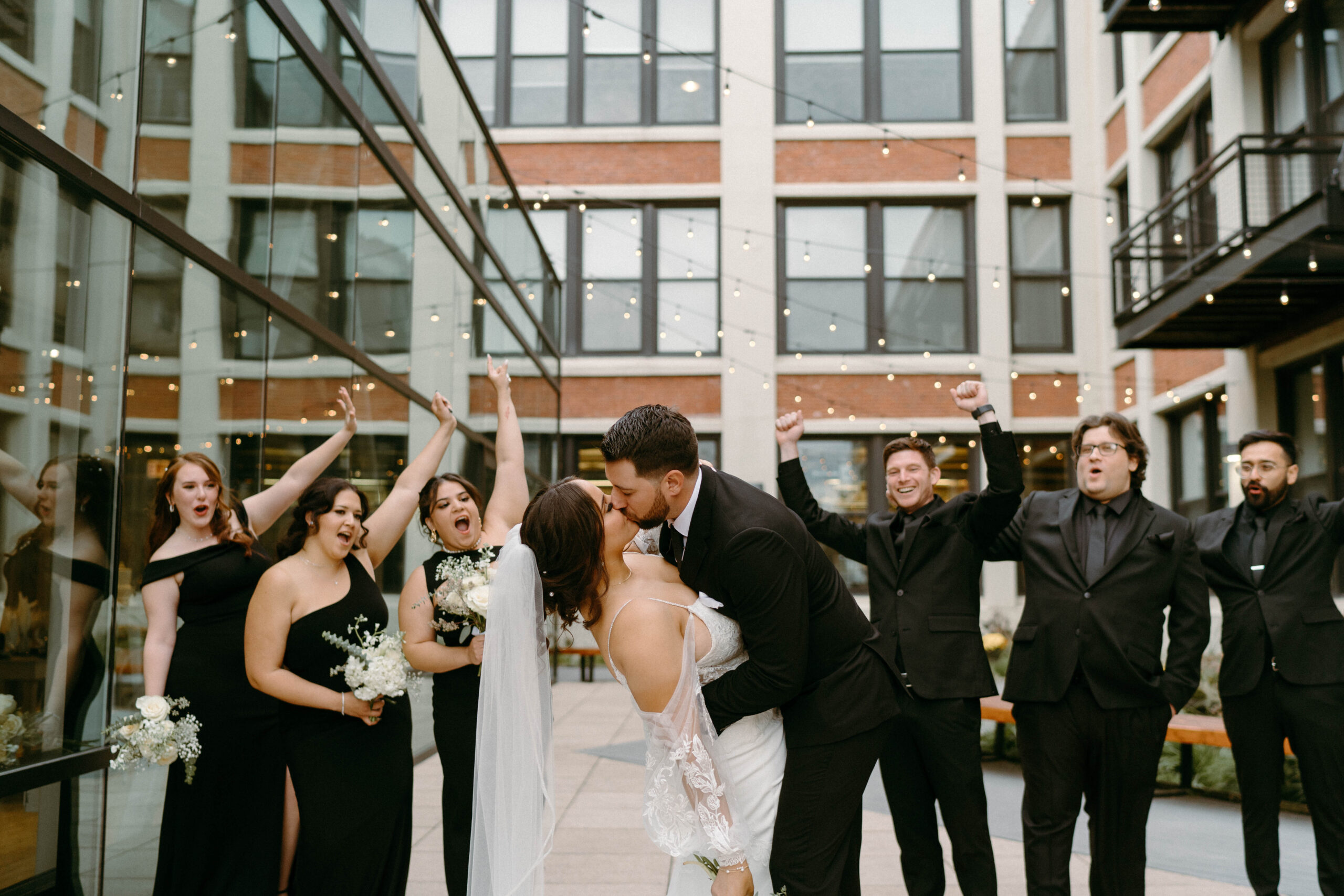 wedding party cheering on bride and groom as they go for a kiss