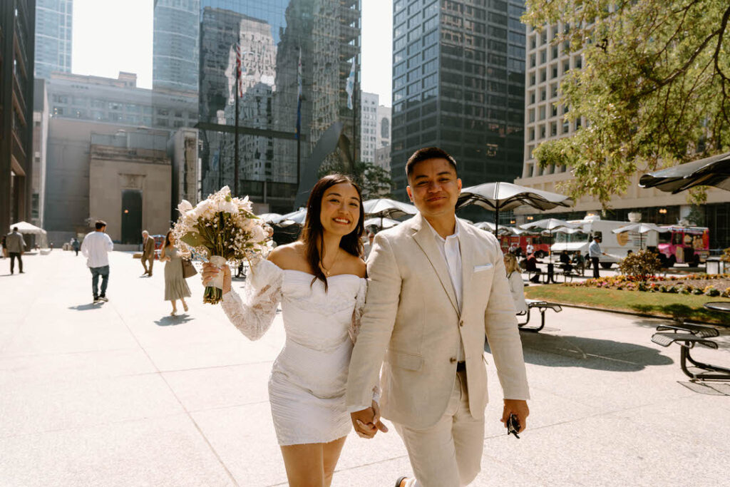a bride and groom holding hands and walking down a sidewalk to elope in chicago city hall