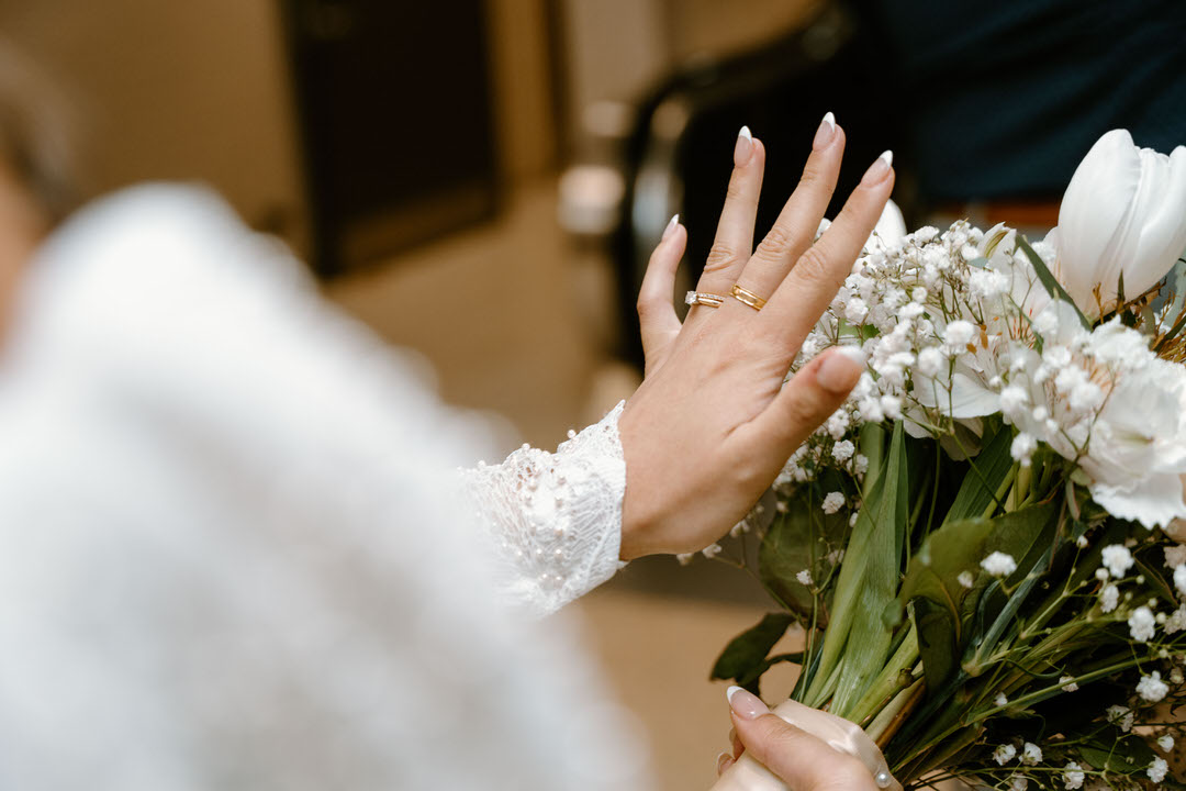 a photo of a womans hand with wedding ring and a bouquet of white flowers on the other hand