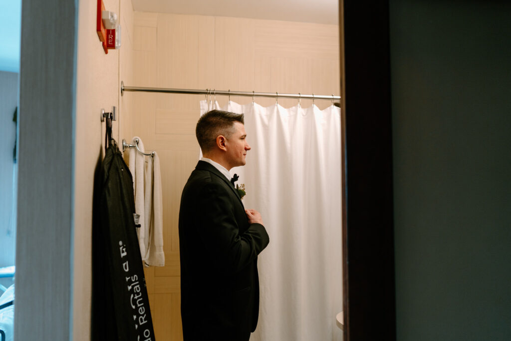 side profile photo of the groom adjusting his tie in the bathroom